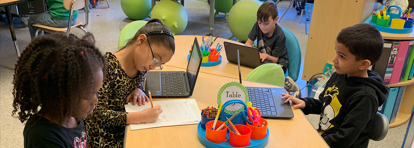 Four young students sitting at a table with laptops